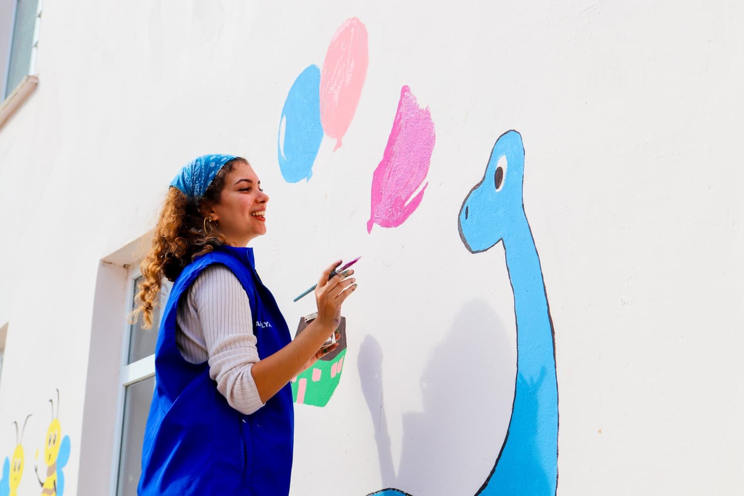 Gönüllü genç, okul duvarına dinozor ve balon figürleri çiziyor